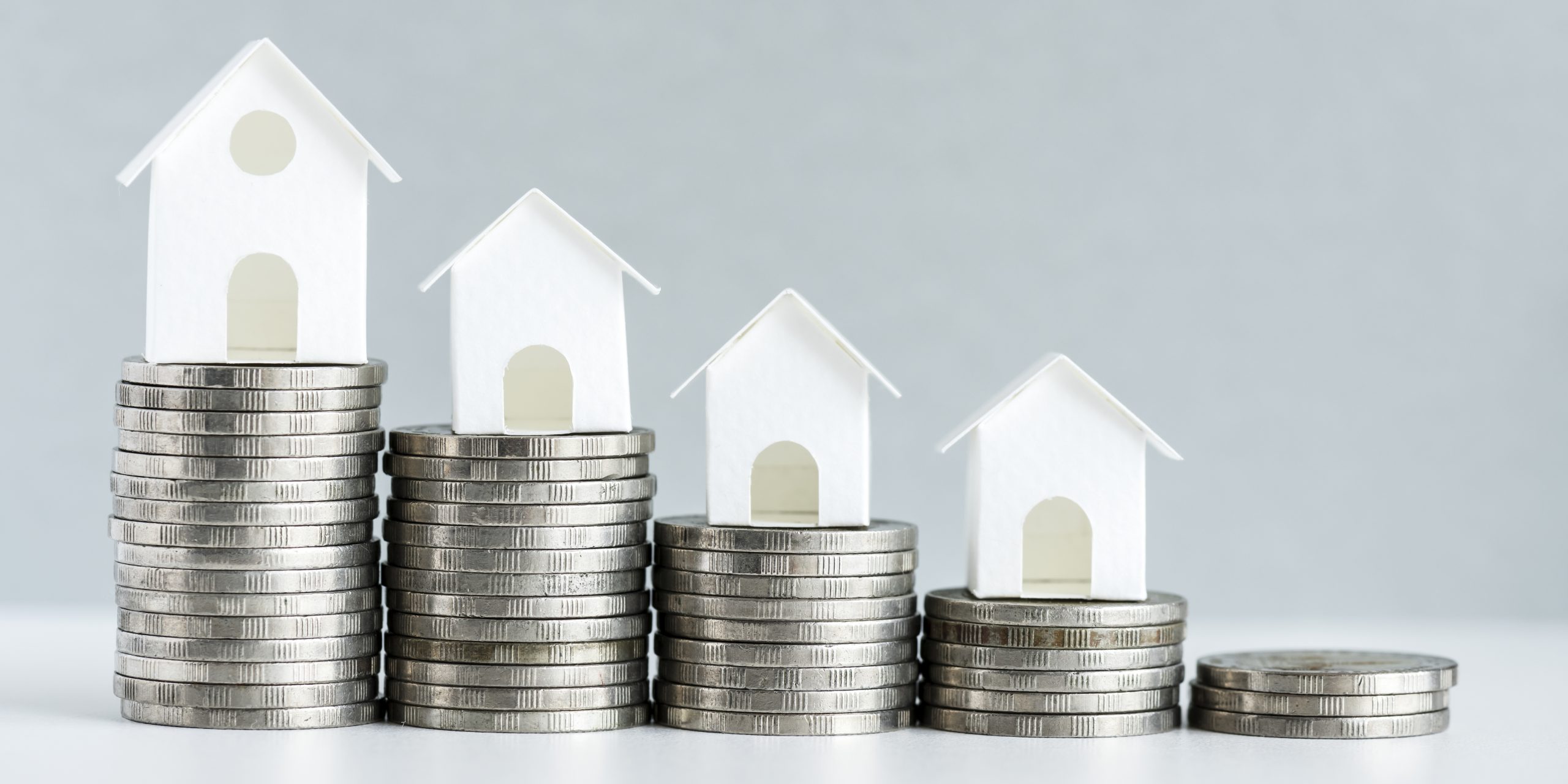 Coins stacked with miniature white houses representing mortgage rates and home financing trends.
