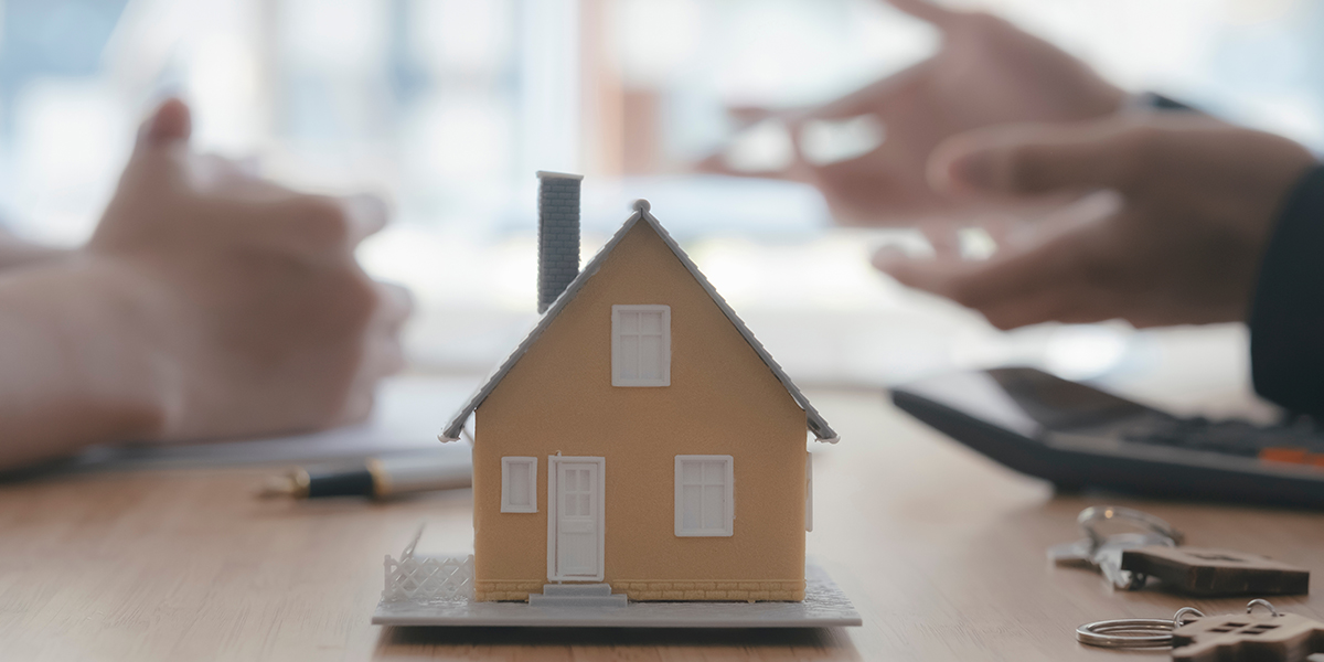 Model house on a table with hands gesturing during a mortgage consultation, emphasizing the post-closing process in home buying.