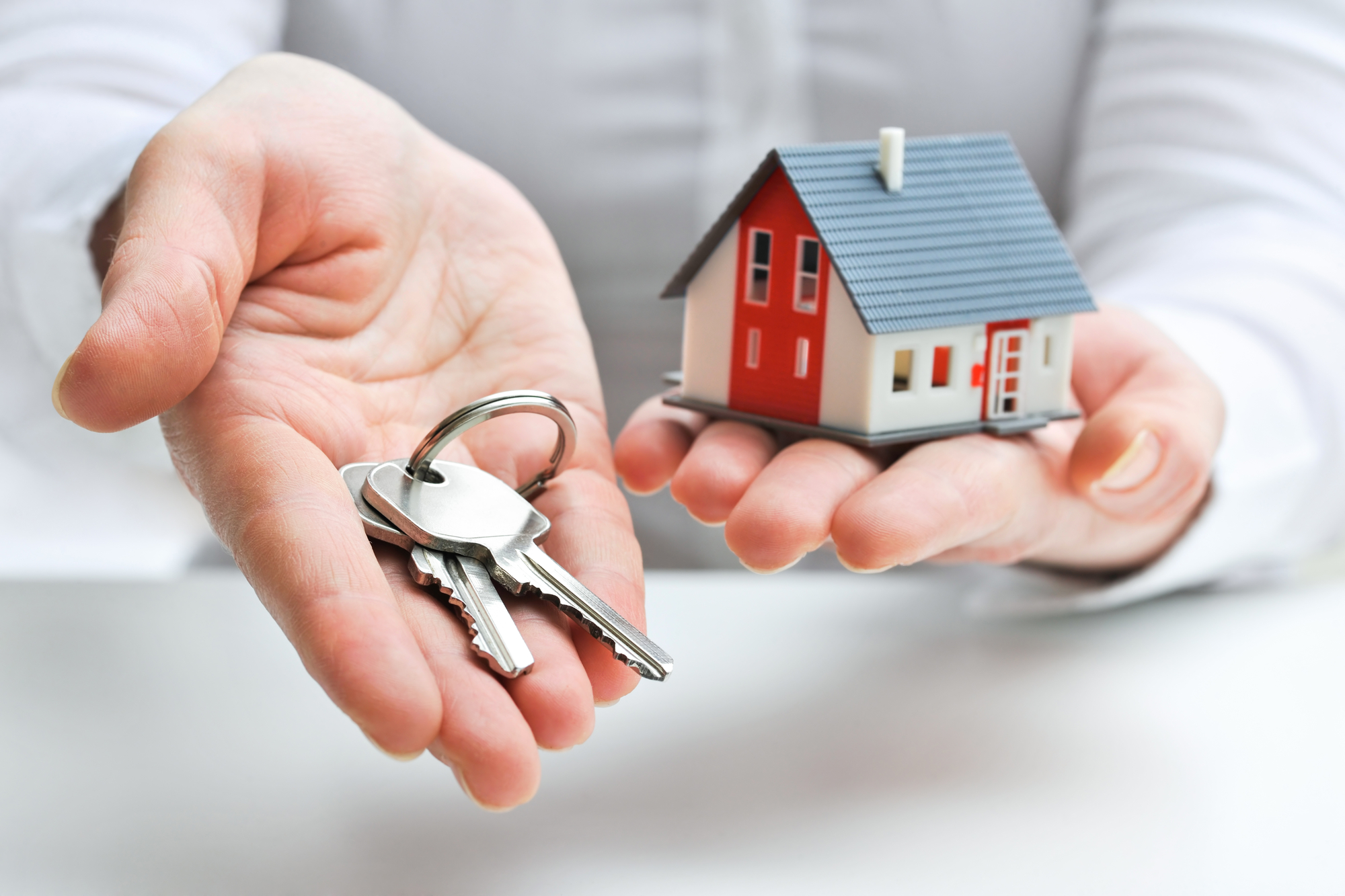 Hands holding house keys and a miniature house model, symbolizing home ownership and the loan process for first-time home buyers.