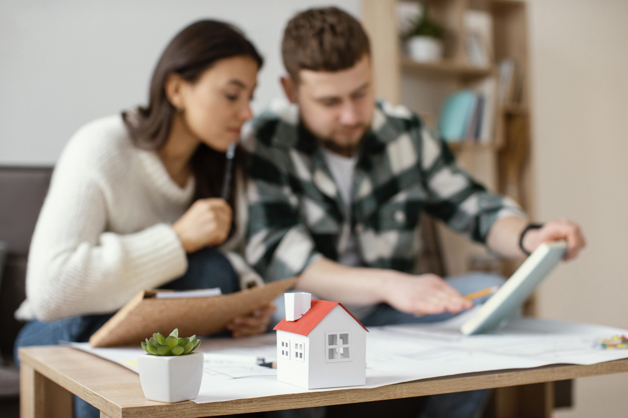Couple discussing mortgage options for home buying, with a miniature house model and documents on a table, symbolizing the mortgage lending process in Elk Grove, CA.