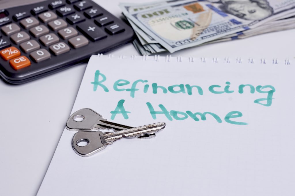 Calculator and keys on notebook with "Refinancing A Home" written, symbolizing mortgage refinancing process and financial decision-making.