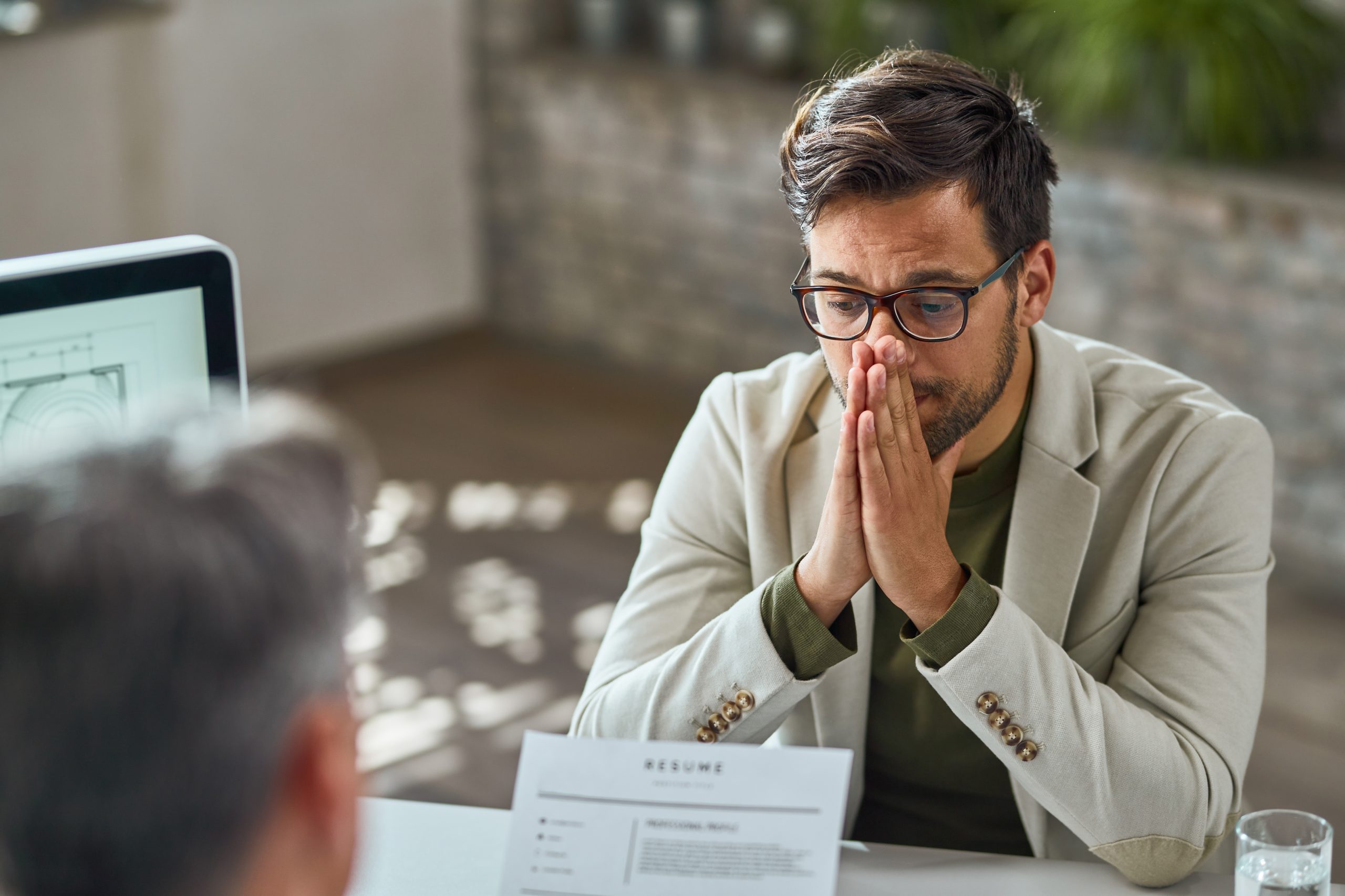 Man with glasses and a worried expression, sitting at a table with a resume, reflecting on loan rejection and exploring alternative solutions.